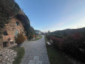 Ein Steinhaus mit rundem Fenster und einer Tür, einem gepflasterten Weg und einer Bank.