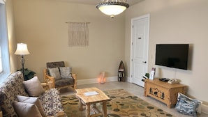 Una sala de estar con sofá, sillón, mesa de centro y televisor sobre un mueble de madera.