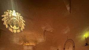 Una habitación tenuemente iluminada con una cama, una lámpara circular fijada a la pared y una lámpara colgante.