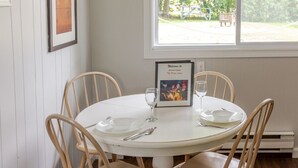 A dining area with a round table, four wooden chairs, a framed welcome sign, and a window with a view of trees. - The Picton Beautiful Couple`s Getaway (Prince Edward)