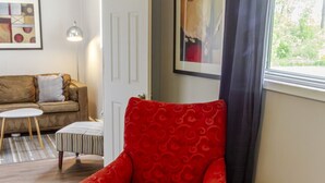 A red armchair in a living room with a wooden floor, a white door, a small round table, and a lamp. - The Picton Beautiful Couple`s Getaway (Prince Edward)