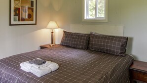 A neatly made bed with a checkered bedspread, a lamp on a bedside table, and a window above the bed. - The Picton Beautiful Couple`s Getaway (Prince Edward)