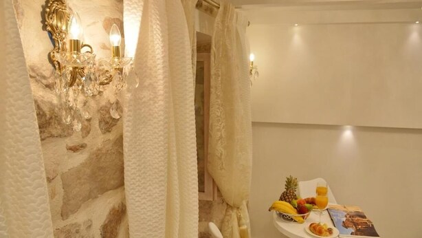 A room with stone walls, a white table with breakfast items, and a wall-mounted light fixture. - Villa Madonna della Strada A 3 (Dubrovnik)