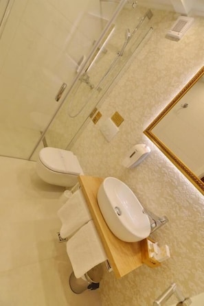 A modern bathroom with a glass shower enclosure, a toilet, a sink with a wooden vanity, and a mirror with a gold frame.