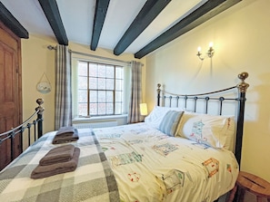 A bed with a checkered bedspread, a bedside lamp, and a window with curtains.