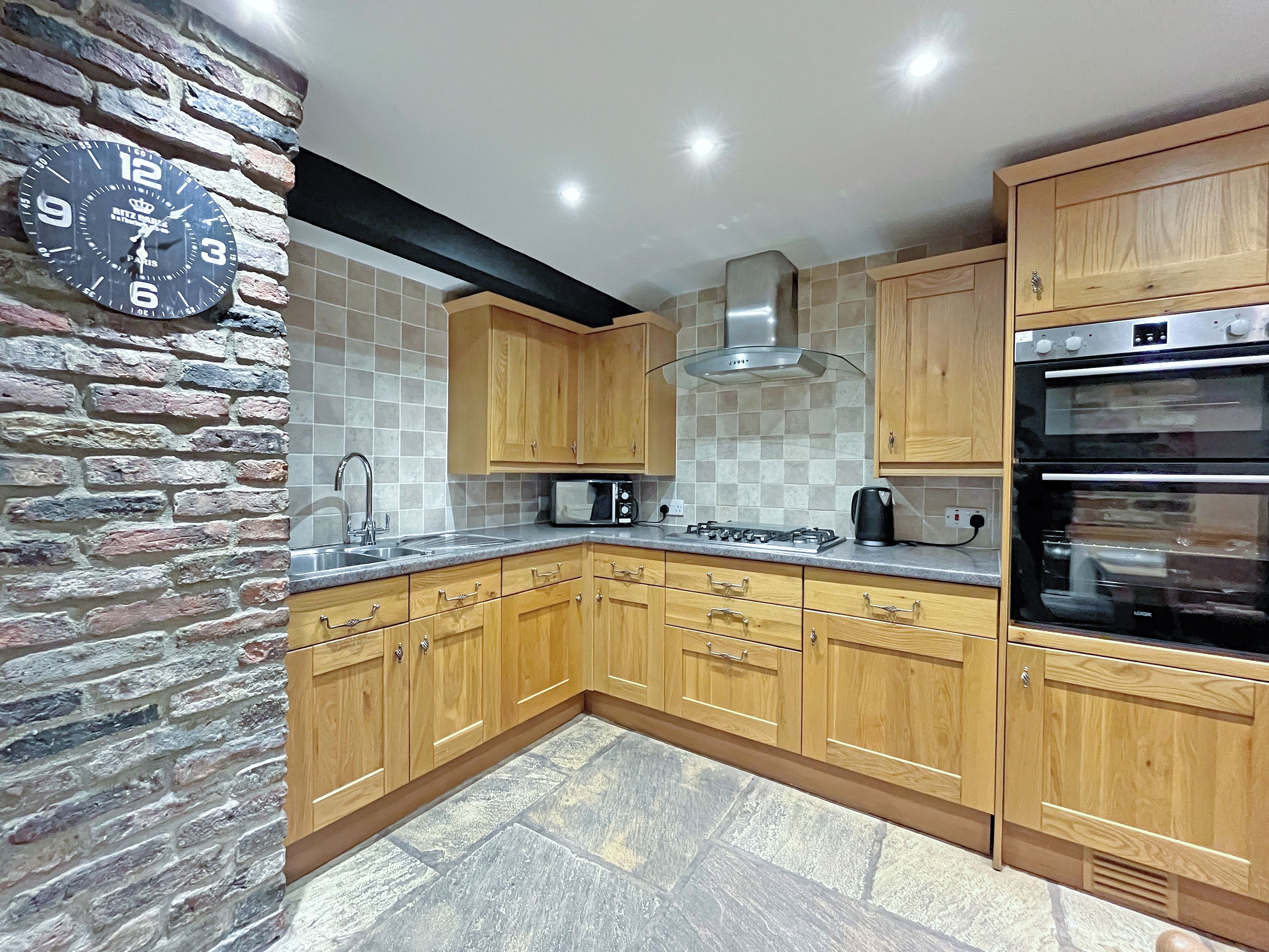 A kitchen with wooden cabinets, a gas stove, a microwave, and a clock on the wall.