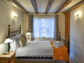 A bedroom with a bed, two bedside lamps, a window with curtains, and a wooden door.