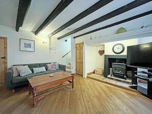 A living room with a sofa, coffee table, fireplace, and wooden beams on the ceiling.