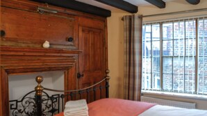 Un lit avec une couvre-lit orange et blanche, une tête de lit en métal et une fenêtre donnant sur des immeubles.