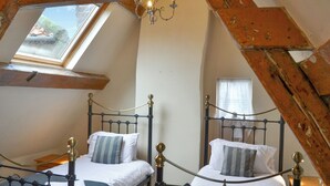 Une chambre avec deux lits, une lucarne, un lustre et des poutres en bois.
