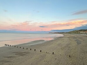 Una playa con una hilera de piedras verticales en primer plano y un mar tranquilo al fondo.