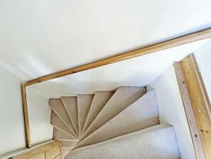 A spiral staircase with a wooden handrail and carpeted steps.