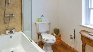 Une salle de bain avec une baignoire, des toilettes et une petite table en bois sur laquelle est posé un objet décoratif.