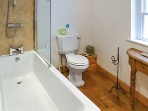 A bathroom with a bathtub, toilet, and a small wooden table with a decorative item. - 3 bedroom accommodation in Whitby (Whitby)