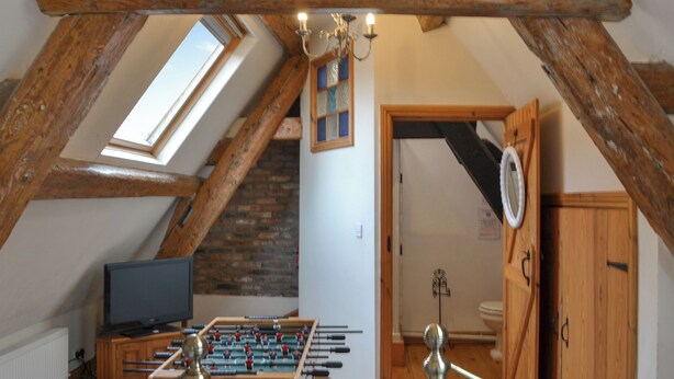 Une chambre mansardée avec un plafond en bois, une table de baby-foot, une télévision et une fenêtre.