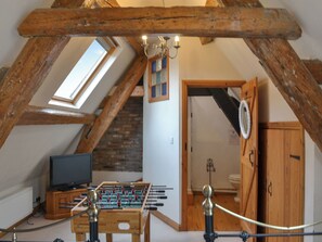 Quarto de sótão com teto de madeira, mesa de pebolim, televisão e uma janela.