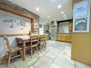 Un comedor con mesa y sillas de madera, una pared de piedra con un reloj y un revoque de azulejos.