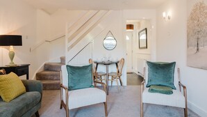 Un salon comprenant un canapé, deux fauteuils, une table à manger avec des chaises, un escalier et un tableau accroché au mur.