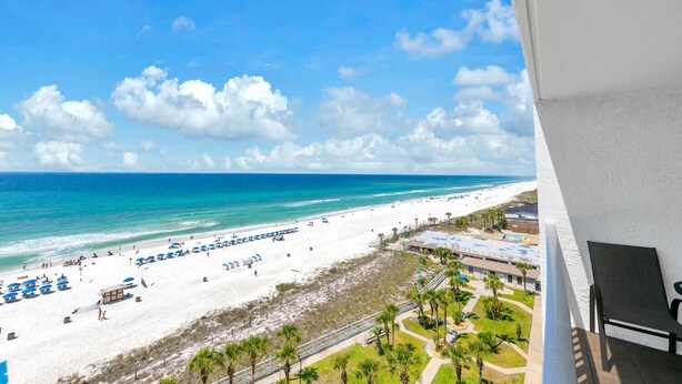 Blick auf den Strand vom Balkon aus, mit blauem Himmel, Sand und einigen Sonnenschirmen.