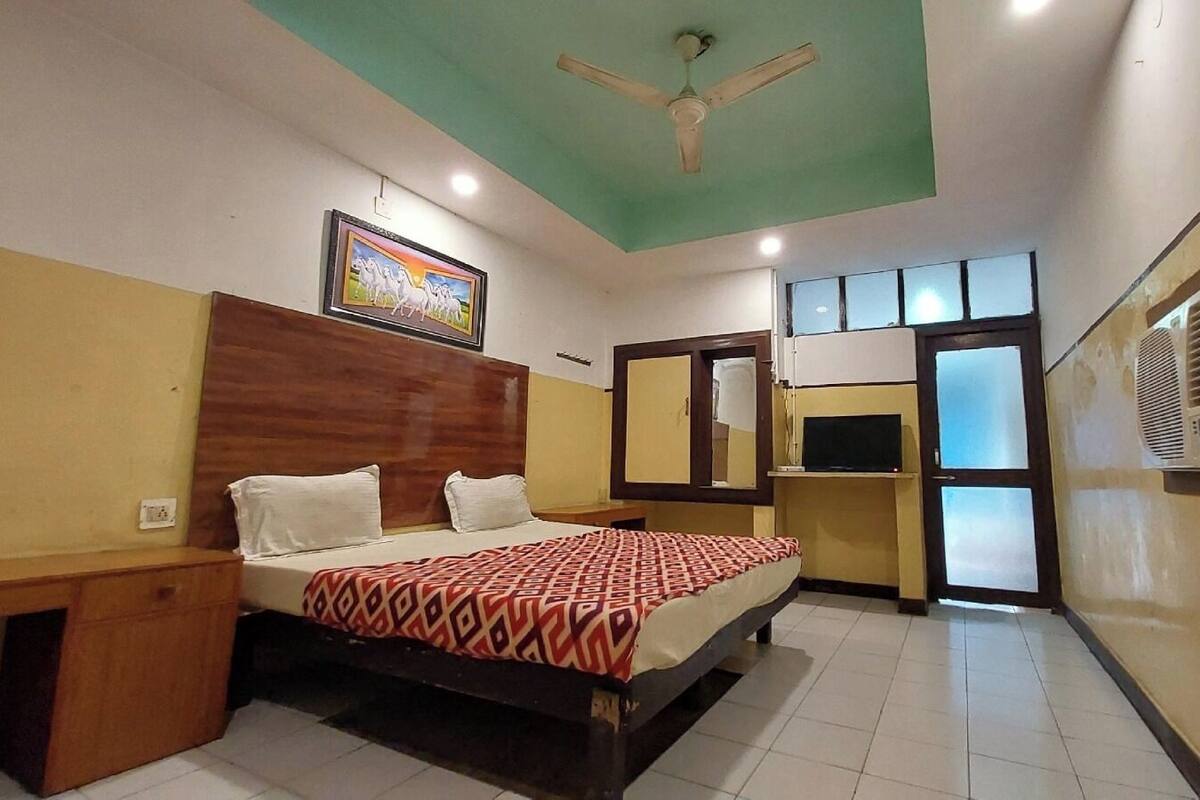 A hotel room with a bed, a desk, a television, a ceiling fan, and a window.