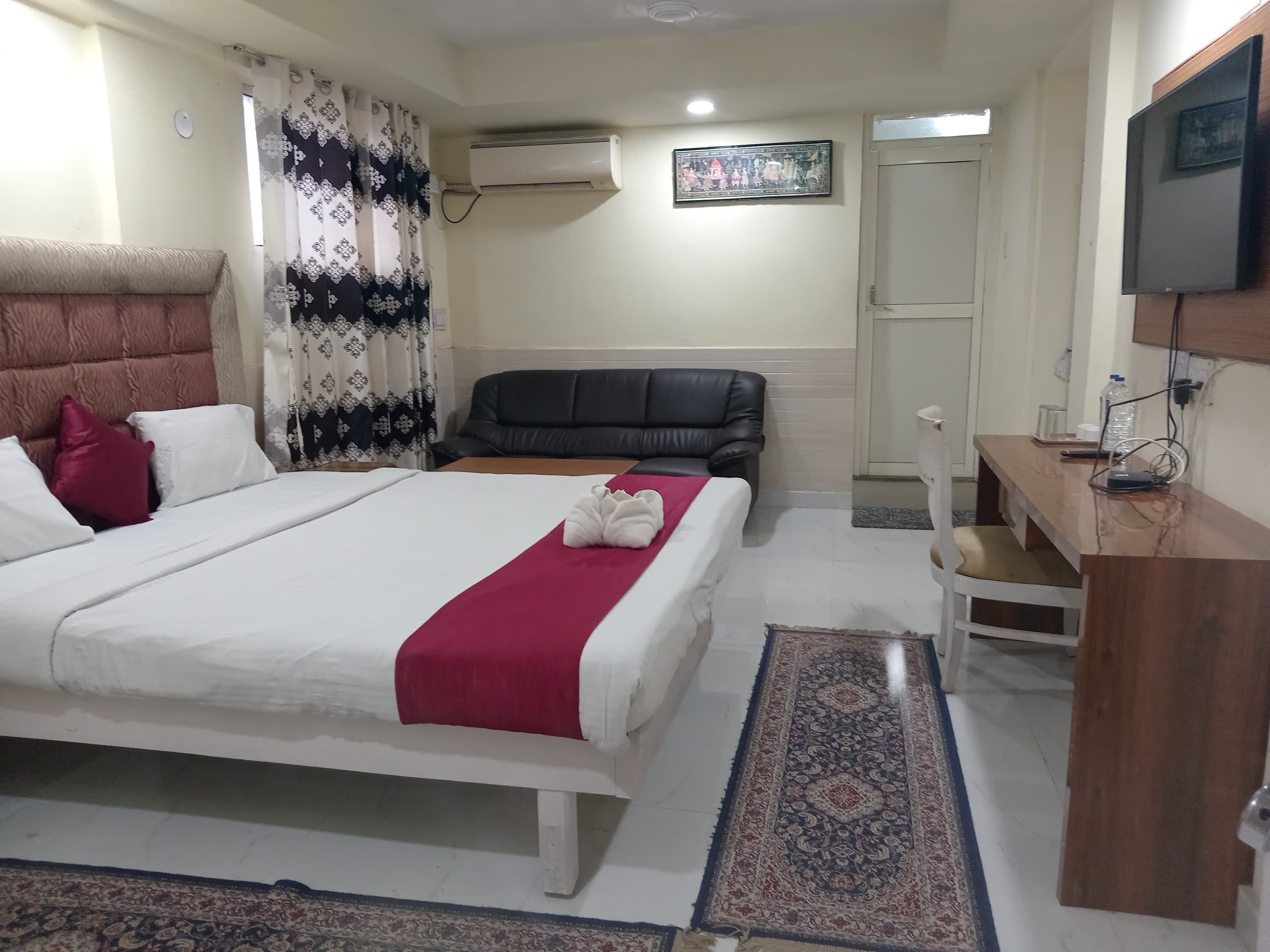 A hotel room with a bed, a desk, a chair, an air conditioner, a television, and a door.