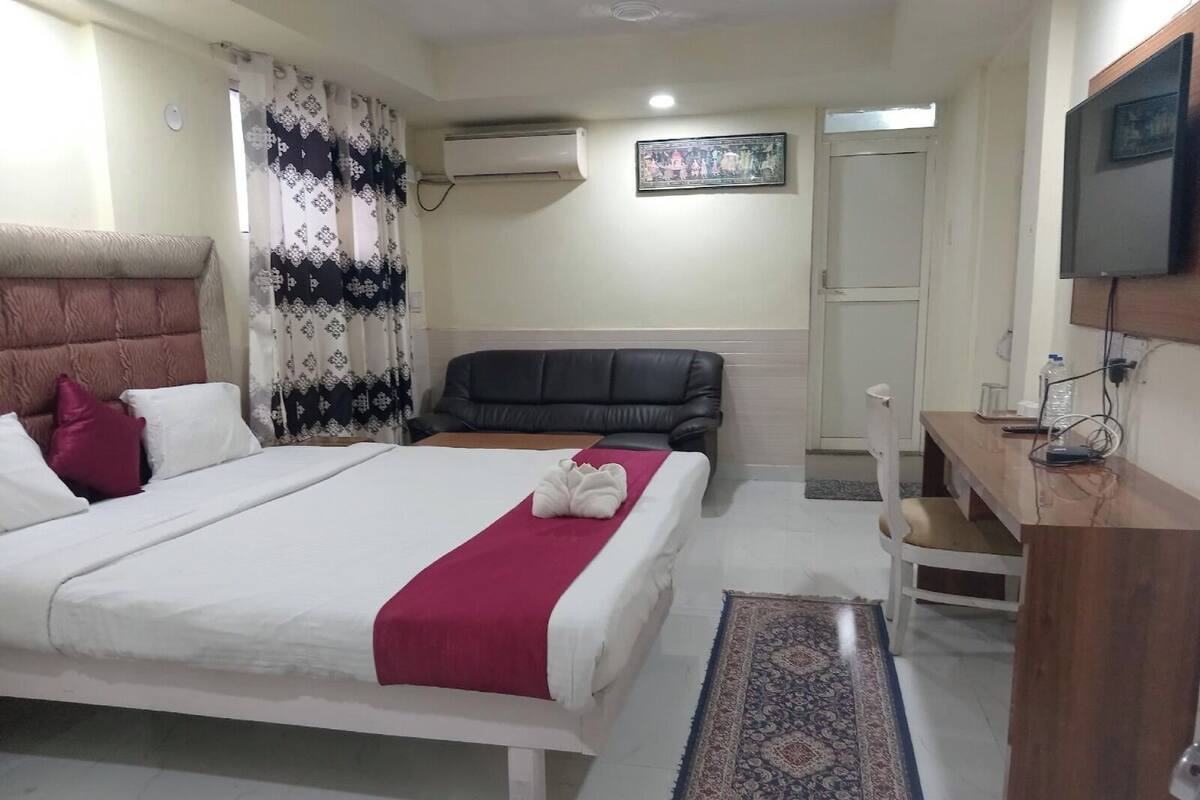A hotel room with a bed, a desk, a chair, a TV, and an air conditioning unit.