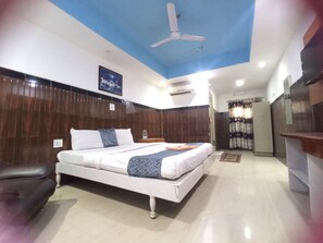 Habitación de hotel con cama, ventilador de techo, equipo de aire acondicionado, panel de pared de madera y ventana con cortinas.