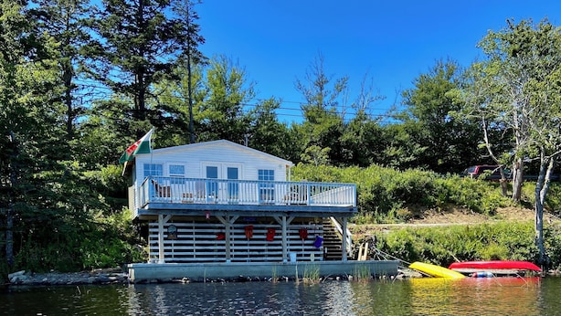 Une cabane avec un quai qui s’avance sur un lac, entourée d’arbres.