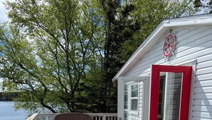 Une terrasse en bois avec des chaises longues et un petit bâtiment doté d’une porte rouge.
