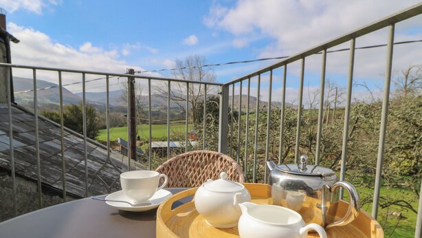 A table set with white cups, saucers, a teapot, a jug, and a tray with food on a balcony with a scenic view. - Cantref House Top Floor (Brecon)