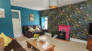 A living room with a blue wall, a black leather sofa, a wooden coffee table, and a colorful floral wallpaper. - Cantref House Top Floor (Brecon)