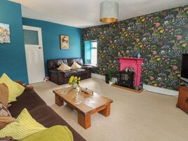 A living room with a blue wall, a black leather sofa, a wooden coffee table, and a colorful floral wallpaper.