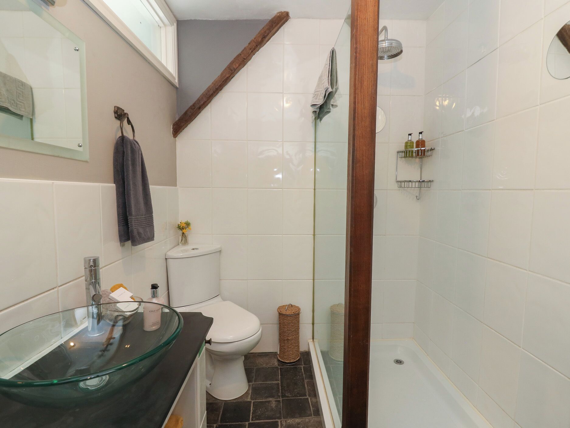 Un baño con lavamanos de vidrio, inodoro blanco y zona de ducha.