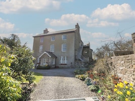 A large, two-story building with a gravel driveway and a stone wall on one side.