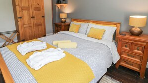 A neatly made bed with a yellow blanket and white towels, wooden furniture, a framed picture on the wall, and a lamp on a nightstand. - Cantref House Top Floor (Brecon)
