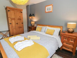 A neatly made bed with a yellow blanket and white towels, wooden furniture, a framed picture on the wall, and a lamp on a nightstand.
