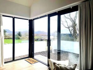 Ein Zimmer mit einer großen Schiebeglasdoor, die auf einen Balkon mit Blick auf eine grüne Landschaft und Berge führt.