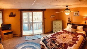 A bedroom with a large bed, a television, a dresser, a desk, and a chair. There is a sliding glass door leading to a balcony.