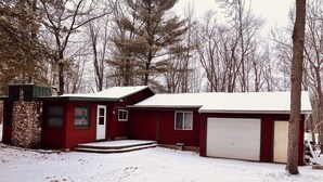 A red single-story house with a garage, a stone wall, and a snow-covered yard.