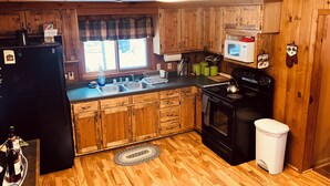 A compact kitchen with wooden cabinets, a black refrigerator, a microwave, and a stove.