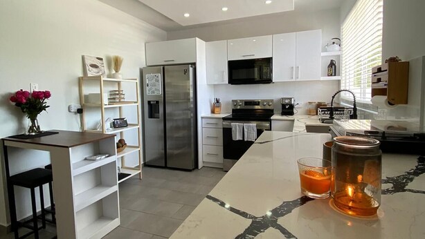 A modern kitchen with white cabinetry, a central island, and a marble countertop. - Sea Breeze Tunnel Hideaway 3 (Quebradillas)