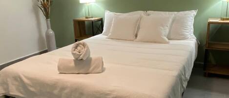 A neatly made bed with a folded towel, two bedside tables with lamps, and three framed botanical prints on the wall.