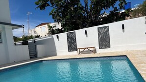 A swimming pool with a tiled edge, a wooden bench, and decorative panels on the wall. - Sea Breeze Tunnel Hideaway 3 (Quebradillas)