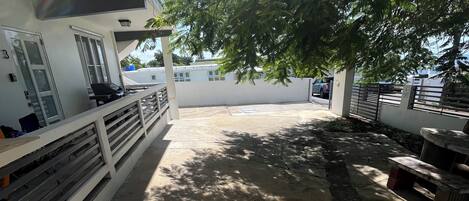 A covered outdoor area with a concrete floor, a white railing, and a tree providing shade.