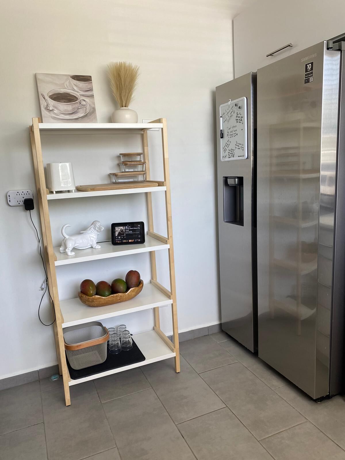 Une cuisine moderne avec un réfrigérateur en acier inoxydable, une étagère en bois contenant des ustensiles de cuisine et un mur blanc.