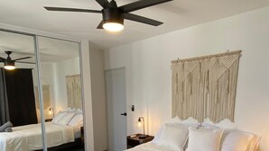 A hotel room with a large bed, a ceiling fan, a mirror, and a wall-mounted macrame decoration. - Sea Breeze Tunnel Hideaway 3 (Quebradillas)