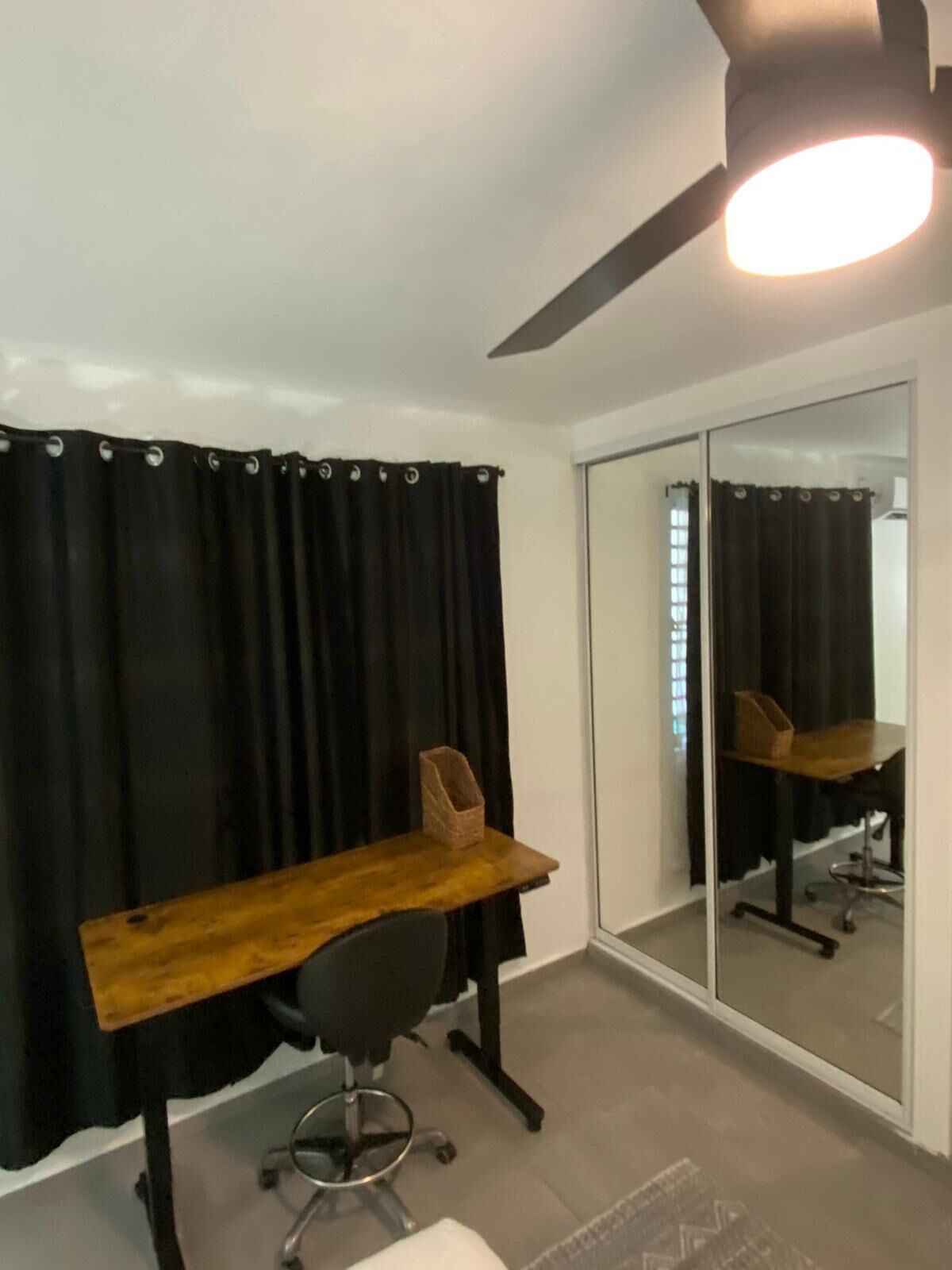 Un espace de bureau moderne avec un bureau en bois, une chaise de bureau noire et un ventilateur de plafond.