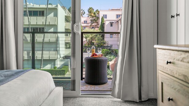 A hotel room with a balcony, a bed, a dresser, and a wicker table with a bottle and glasses. - Seize the Day by Gather: 2BR Retreat w/ Views & Parking (La Jolla)