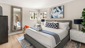 A modern bedroom with a large bed, a nightstand, a mirror, and artwork on the walls. - Seize the Day by Gather: 2BR Retreat w/ Views & Parking (La Jolla)