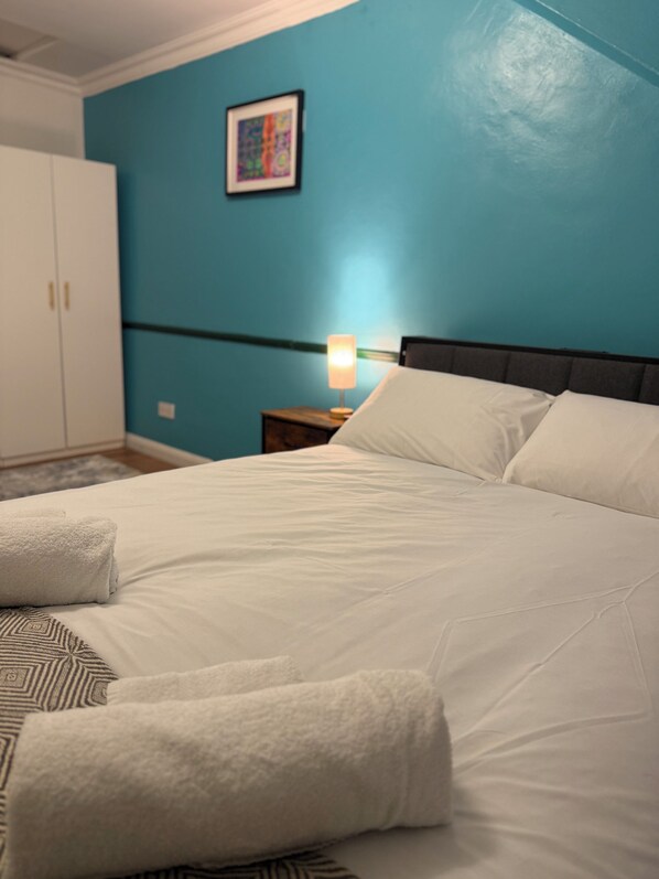 A neatly made bed with white linens and pillows, a bedside lamp, and a framed artwork on the wall.